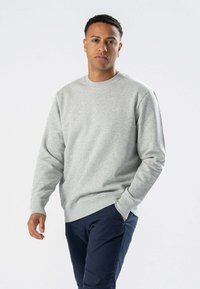 Grå sweatshirt med rund hals, lange ærmer og ribbede manchetter, parret med marineblå bukser. Blødt stof, afslappet pasform, minimalistisk design.