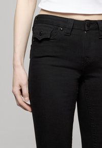 Zwarte denim jeans met een slanke pasvorm, voorzien van voor- en achterzakken, metalen hardware en subtiele stiksel details. Soepele textuur.