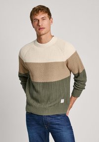 Jersey de punto con un diseño de bloques de color en crema, beige y verde. Tejido texturizado con puños y dobladillo acanalados, etiqueta en la parte inferior izquierda.