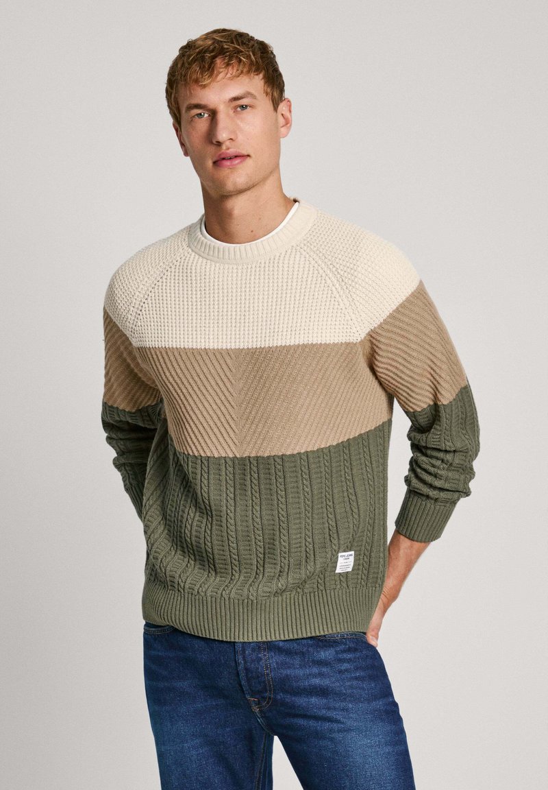 Jersey de punto con un diseño de bloques de color en crema, beige y verde. Tejido texturizado con puños y dobladillo acanalados, etiqueta en la parte inferior izquierda.