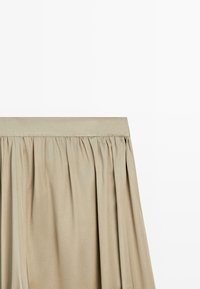 Jupe plissée beige avec une large ceinture, fabriquée en tissu lisse, présentée sur un fond blanc uni.