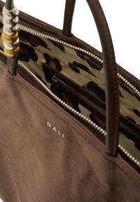 Sac en suède marron avec des poignées en cuir. L'intérieur présente une doublure en imprimé léopard marron et tan, ainsi qu'une poche zippée. Logo "NALÍ" à l'extérieur.