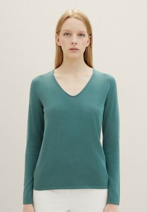 Pull en teinte sarcelle à manches longues avec un col en V, confectionné dans un tissu doux et lisse. Il présente une coupe légèrement décontractée et des bords côtelés.