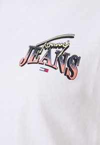Bílý bavlněný tričko s multicolor logem "Tommy Jeans", s retro stylem a výraznými gradacemi v růžové, modré a žluté.