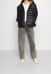 Černá prošívaná péřová bunda s horizontálním prošíváním, oranžovým vnitřkem, doplněná o šedé džíny s vysokým pasem a béžové boty na blokovém podpatku.