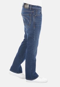 Jeans de mezclilla azul con corte recto; presentan costuras naranjas, un parche de marca en la cinturilla y un ligero desgaste en la tela.