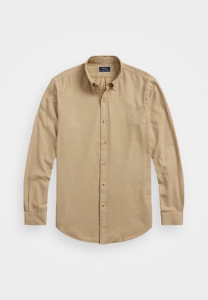 Beige long-sleeved button-down shirt with a classic collar, subtle embroidered logo, and rounded hem. Soft cotton fabric with a smooth texture.