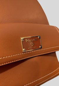 Borsa a tracolla in pelle marrone con placca logo dorata, cuciture decorative e una texture liscia con chiusura a patta.