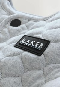 Hallitatud halli kangast, millel on tekstuuriga muster. Must silt valge lõigatud tekstiga "BAKER by Ted Baker". Ringikujuline must nupuvajutus.
