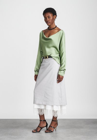 Πράσινη σατινένια μπλούζα με ντραπέ λαιμόκοψη, συνδυασμένη με μια ανοιχτό γκρι φούστα με δαντελένια τελειώματα. Μαύρες γόβες με λουριά ολοκληρώνουν το σύνολο.