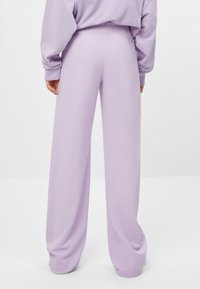 Lavender wijde pijpen broek met een gladde stofafwerking en een elastische tailleband, getoond vanuit de achterkant, gecombineerd met een bijpassend oversized top.