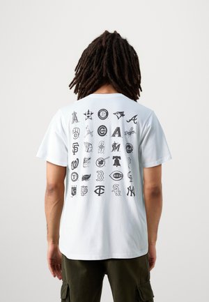 Camiseta de algodón blanca con un estampado gráfico de varios logotipos de equipos deportivos en negro en la parte posterior, con mangas cortas y un cuello redondo.