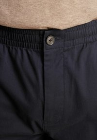 Pantalones de cintura elástica en color navy con cierre de botón, que presentan una textura suave y un brillo sutil. La imagen en primer plano muestra el detalle de la costura y la cinturilla.