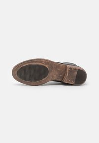 Suela de zapato de cuero negro con una suela de goma desgastada. Presenta un patrón de zigzag texturizado y acentos suaves. Se pueden ver ligeras manchas de suciedad.