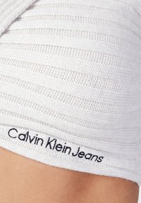 Tessuto a maglia bianco con strisce orizzontali e una finitura testurizzata. Presenta il logo "Calvin Klein Jeans" ricamato in nero all'orlo.