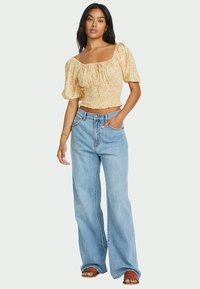 Yellow floral cropped top with puff sleeves and smocked bodice paired with light blue wide-leg jeans and brown flat sandals.