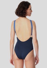 Maillot de bain une pièce bleu marine avec un dos décolleté et de fines bretelles bleues, comportant une accent blanc en haut et une texture lisse.