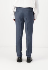 Blaue maßgeschneiderte Hosen aus strukturiertem Stoff, mit geradem Bein und zwei Gesäßtaschen, kombiniert mit schwarzen Schuhen.