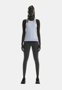 Sport-Tanktop aus hellblauem Stoff, kombiniert mit dunkelgrauen Leggings. Das Model steht frontal und trägt schwarze Sportschuhe.