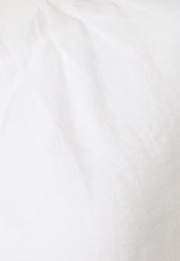 Cuscino bianco con una texture liscia e morbida e leggere pieghe; presenta linee pulite e una forma piena, adatto per arredamenti casual o moderni.