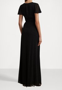 Svart maxiklänning med korta, genomskinliga ärmar, figursydd överkropp och en svävande nederdel. Har en mjuk textur och en diskret dragkedjestängning i ryggen.