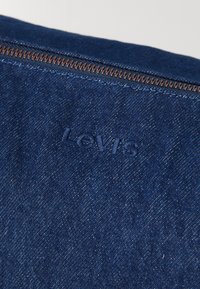 Pochette en denim bleu foncé avec fermeture éclair, logo Levi's en relief et détails de couture visibles.