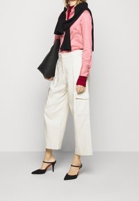Camicia di satin rosa chiaro, polsini in maglia rossa, sciarpa nera, pantaloni cargo bianchi, décolleté slingback neri con punta affusolata e suola rossa. Borsa tote nera.