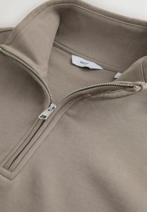 Beež kvartstõmblukuga pullover hõbedase tõmblukuga ja nähtava "NEXT" brändisildiga kaeluse siseküljel.