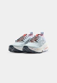 Baskets de course bleu clair avec un design texturé, dotées d'une semelle blanche mouchetée, de lacets intégrés et de détails roses sur la languette et le talon.