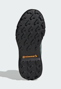 Svart gummisåle med et teksturert mønster som har piltformede knaster. "Continental"-logo i oransje nær hælen.