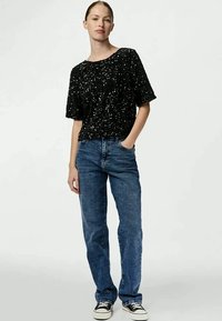 Top de mangas curtas preto com lantejoulas emparelhado com jeans de ganga azul de cintura alta e ténis pretos, apresentando um corte descontraído e design de perna reta.