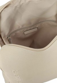 Interno di una borsa in tessuto beige con una tasca con zip. Presenta una texture liscia e un branding sottile sulla fodera. Chiusura con zip nella parte superiore.