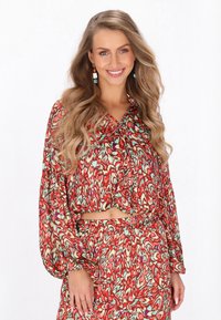 Rode bloempatronen blouse met lange mouwen, V-hals en strikdetail, gecombineerd met een bijpassende hoge taille rok in een vergelijkbaar patroon.