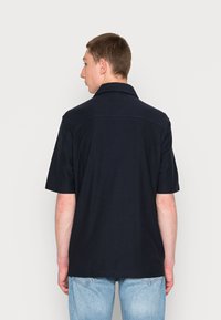 Camisa polo azul-marinho de manga curta com colarinho estruturado, corte reto e textura de algodão suave, combinada com jeans azul-claro.