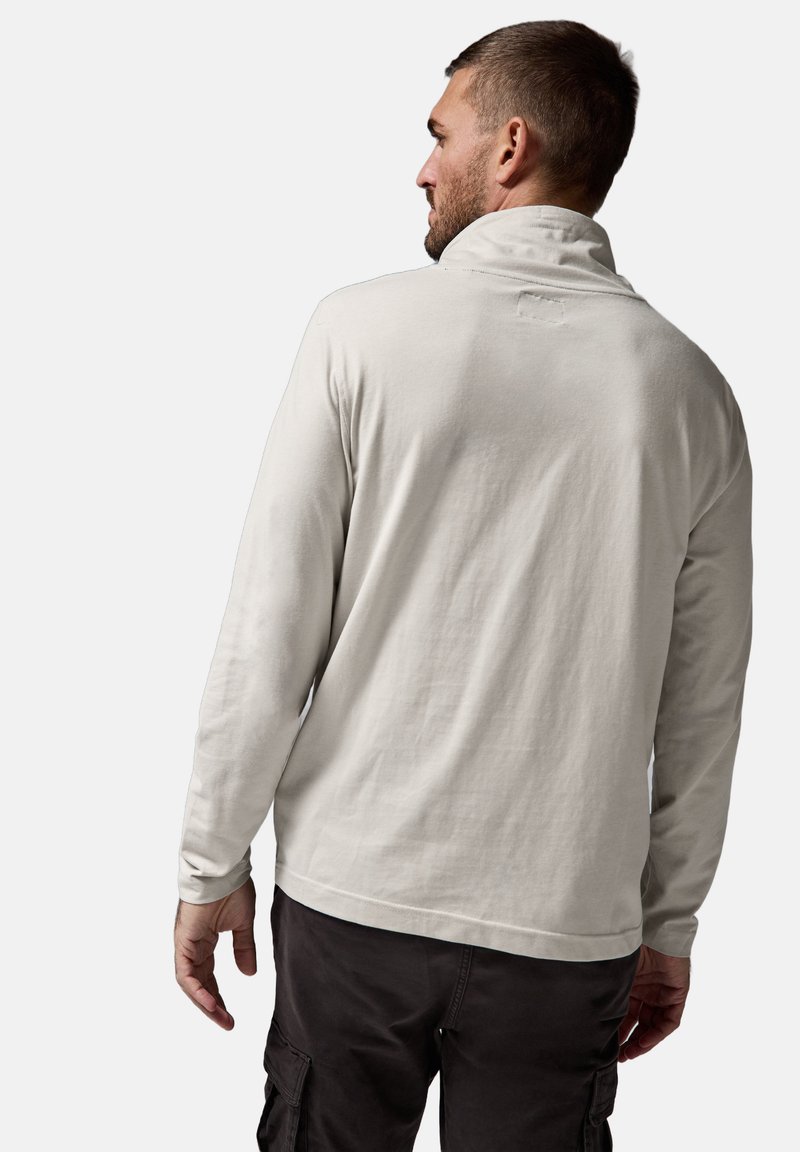 Suéter de manga larga gris claro con cuello alto, textura suave y detalles de costura mínimos, combinado con pantalones cargo oscuros.