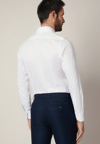 Biała koszula z długim rękawem, klasycznym kołnierzykiem, gładką fakturą i dopasowanym krojem, zestawiona z ciemnoniebieskimi, dopasowanymi spodniami z dwoma tylnymi kieszeniami.