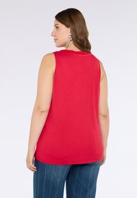 Top senza maniche rosso con collo rotondo, vestibilità morbida, texture liscia e spacchi laterali, abbinato a pantaloni a palazzo blu a righe.