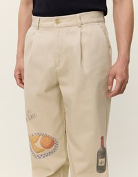 Μπλε βαμβακερό παντελόνι με άνετη εφαρμογή, που διαθέτει εκτύπωση πορτοκαλιών και σχέδιο φιάλης κρασιού στο αριστερό πόδι. Λεπτομέρεια με κουμπί.