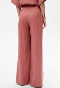 Jasnoróżowe spodnie o szerokich nogawkach wykonane z gładkiego materiału, z elastycznym paskiem w talii i swobodnym krojem, z bocznymi rozcięciami u dołu.