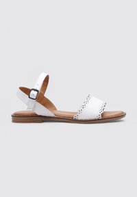 Sandal de piel blanca con tira en el tobillo asegurada con un hebilla negra, diseño recortado en la banda superior y suela plana marrón.