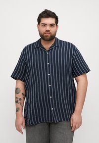 Camisa de botones a rayas marino con un corte relajado, mangas cortas y cuello tipo polo, que presenta rayas verticales en blanco y azul claro.
