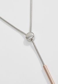 Silver-tone necklace with a round metallic clasp, featuring a sleek, flexible chain and a rose gold accent in a slender tube shape.