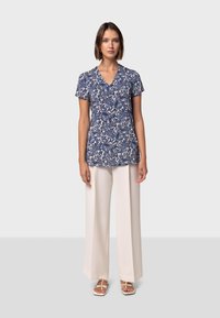 Mörkblå kortärmad topp med paisleymönster, parat med krämfärgade byxor med vida ben och vita sandaler. Har en V-ringning.