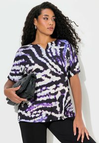 Top de manga corta en patrón tie-dye negro, morado y blanco; diseño de cuello en V; tejido ligero; combinado con un bolso de mano negro.