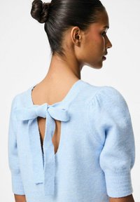 Ljusblå stickad tröja med puffärmar, djup V-back och en rosett vid halsringningen. Mjuk textur, avslappnad design.