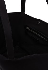 Interno della borsa a spalla nera in tela con una texture liscia, dotato di una tasca con zip e di sottili manici in tessuto. Design pulito con dettagli minimi.