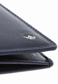 Gros plan sur le coin d'un portefeuille en cuir noir avec une couture fine et un petit logo argenté sur une surface texturée.