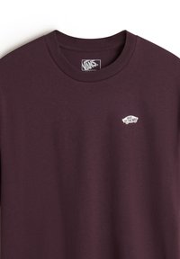 Camiseta de algodón morada con cuello redondo y mangas cortas, que presenta un logo blanco de "Vans Off the Wall" en el pecho. Textura suave.
