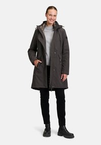 Dark grey waterproof parka with a hood, two side pockets, zipper closure, and a slightly fitted silhouette. Worn over a light grey sweater.