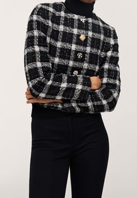 Sort og hvidternet cropped jakke med en tekstureret stof, der har runde guldknapper og ribbede manchetter og kant.